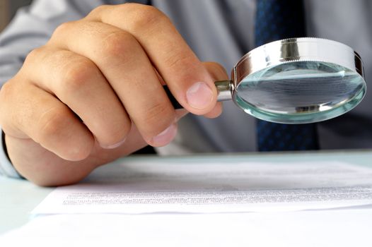 Businessman looking through a magnifying glass to documents