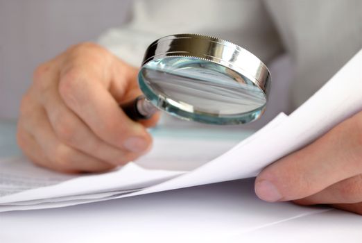 Businessman looking through a magnifying glass to documents