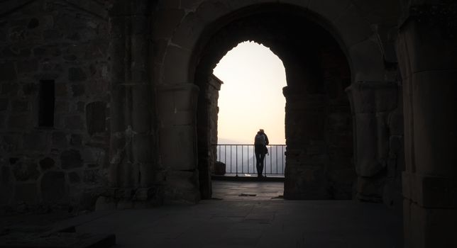 one tourist on a balcony in an old castle in Georgia looks at the sunset in the mountains