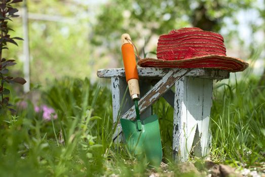 garden shovel, a bench and a hat on a bed of green plants