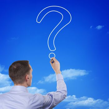 Conceptual image of a young man with his back to the camera drawing the outline of a question mark in the blue sky