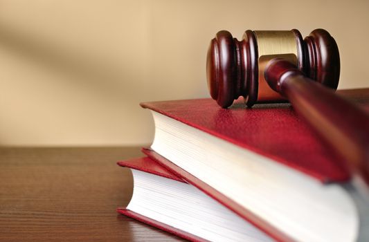 Wooden judges gavel with a brass band around the head resting on top of a closed red law book with shallow dof and copyspace