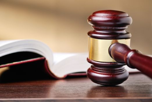 Judges wooden gavel with a brass band around the mallet standing upright on a wooden counter top alongside a law book conceptual of judgements and law enforcement