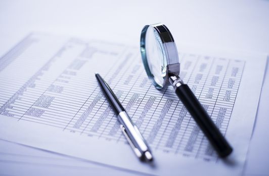 conceptual image analysis of financial statements, documents, dollars, magnifying glass and pen on office desk