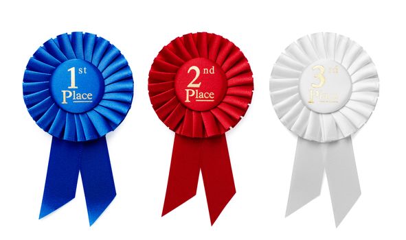 1st, 2nd and 3rd Place pleated ribbon rosettes or badges in blue, red and white respectively with central text isolated in a row on a white background, overhead view