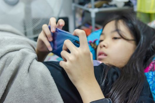 An Asian girl is addicted to a cell phone game lying on a bed.Focus on the hand