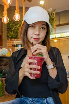 Beautiful Asian woman wearing a black shirt, wearing a hat, drinking strawberry juice