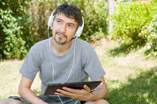 young man holding a tablet with headphones, outdoor