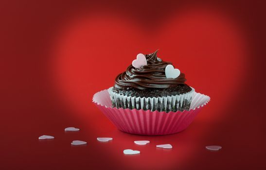 Chocolate cupcake with nice chocolate icing garnish with pink eatable hearts on red background