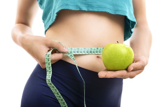 Portrait of woman in sportswear measuring her slim waist and body with a measuring tape and holding a fresh green apple, isolated on white background. Health care, dieting, weight loss or beauty concept.