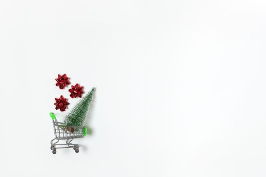 Christmas snow covered fir and red bows for gift in toy shopping cart on white background, copy space. New Year, sales, online shopping concept. Horizontal, flat lay. Minimal style. Top view.