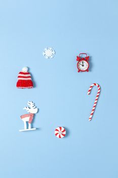 Simple creative Christmas composition. Candy cane, deer, hat, snowflake, red clock on blue background, copy space. Minimal style. Top view. Vertical. For social media, greeting card, office supplies.