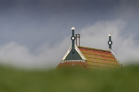 Colorful gable of a farm behind a green dike in northern Netherlands 
