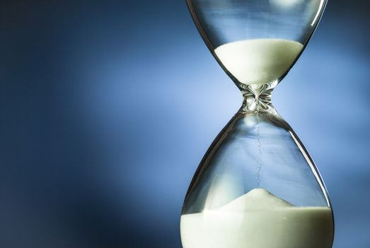 Sand running through an hourglass or egg timer in a concept of time management, countdown or deadline over blue with copyspace