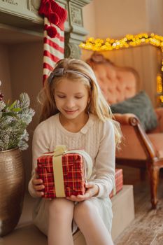 Cute teen girl looking on present near Christmas tree 