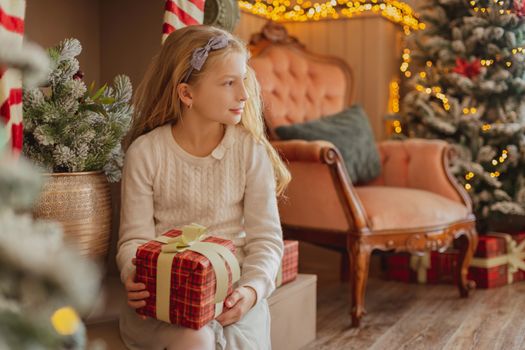 Cute teen girl with present near Christmas tree looking aside