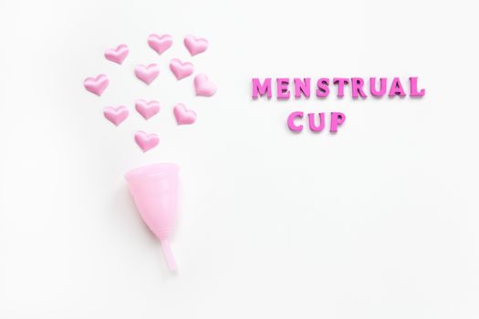 Pink menstrual cup on white background with small hearts and inscription. Concept zero waste, savings, environmental conservation, sustainable lifestyle. Feminine hygiene product, flatlay. Horizontal.