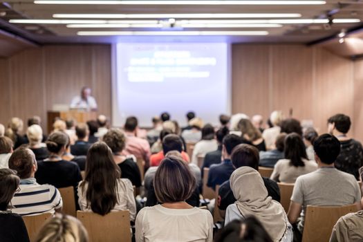 Speaker giving a talk in conference hall at business event. Audience at the conference hall. Business and Entrepreneurship concept. Focus on unrecognizable people in audience.