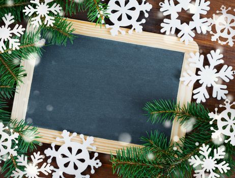 Beautiful Christmas card in vintage style. Blank chalkboard surrounded by green fir branches and white felts snowflakes with copy-space