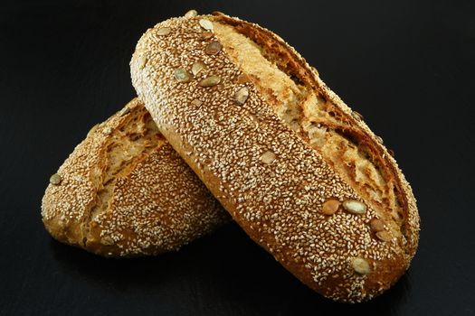 In images Two whole homemade buckwheat loaf bread with buckwheat flour on black textured background. Top view or flat-lay. Copy space. Low key