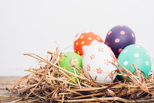 Beautiful Easter multi color egg in straw on wooden background, Easter day concept