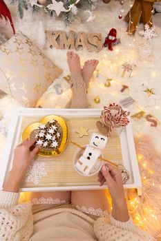 Enjoying hot chocolate with floating marshmallow snowman and tasty gingerbread in front of the Christmas tree with pretty Christmas decorations scattered around.