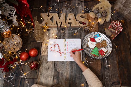 Writing out a Christmas list on rustic timber floor with Christmas decorations, fairy lights  and festive gingerbread.  Christmas scene background