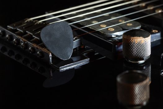 Black guitar pick on black electric guitar in darkness. Concept of rock music style.