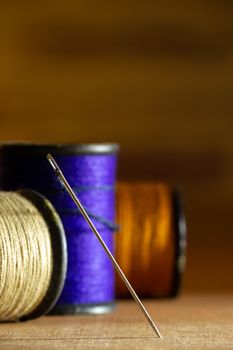 Needle and threads on wooden table. Closeup and copy space for text. Concept of tailor or Designer.