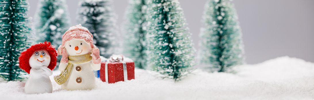 Two small cute snowmen friends with gifts in forest under falling snow