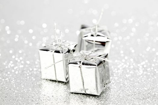 Decorative silver boxes with holiday gifts on shiny glitter background