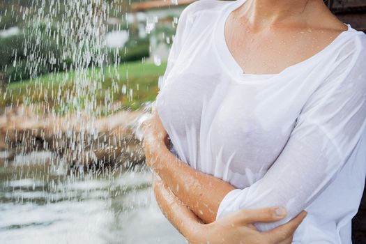 Attractive young female in wet blouse looking away while standing near splashing clean water in resort