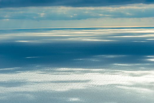 Calm sea surface in the rays of the sun breaking through the clouds