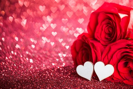 Three red roses and decorative hearts over bokeh glittering background