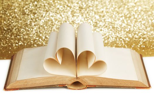 Pages of open book rolled in heart shape on glitter background
