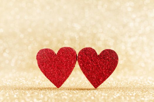 Two small handmade red glitter hearts on bright golden lights bokeh background Valentines day card