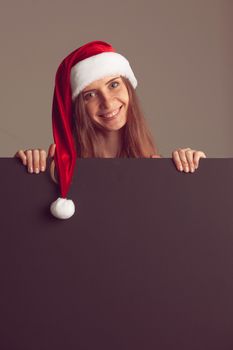 Woman wearing santa christmas hat holding and pointing blank billboard or placard sign copy space for text advertising