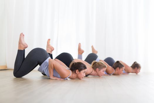 Group of young sporty sexy women in yoga studio, practicing yoga lesson with instructor, forming a line in Shishosana bent puppy dog asana pose. Healthy active lifestyle, working out indoors in gym.