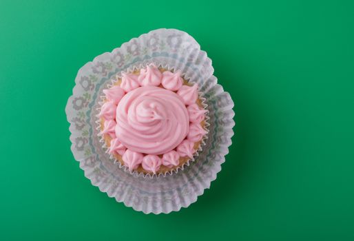 Delicious sweet vanilla cupcake with pink icing sugar, green background