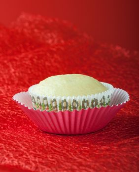 Baked vanilla cupcake on decorative paper mold, red background