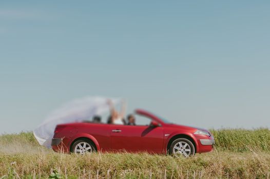 Bride and groom at a photo session in the nature. Moving fast red car with veil outside