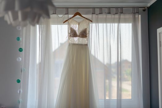 Bridesmaid helping slender bride lacing her wedding white dress, buttoning on delicate lace pattern with fluffy skirt on waist. Morning bridal preparation details newlyweds. Wedding day moments, wear.