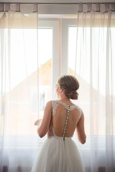 Bridesmaid helping slender bride lacing her wedding white dress, buttoning on delicate lace pattern with fluffy skirt on waist. Morning bridal preparation details newlyweds. Wedding day moments, wear.