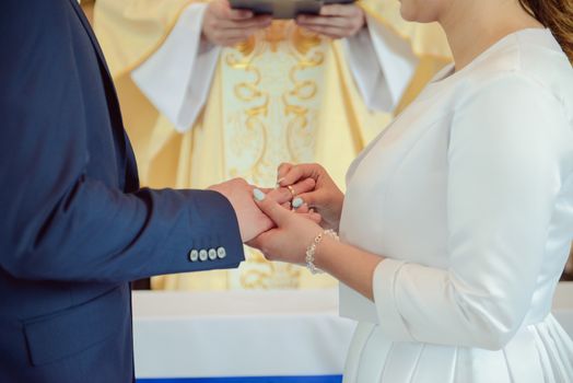 the bride and groom during the wedding ceremony put wedding rings on their fingers.