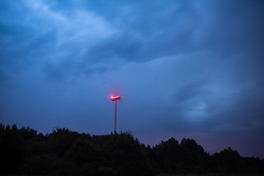 Wind turbines on a dramatic dark blue clouds in the sky. Storm ahead is coming. Red warning light on the windmill