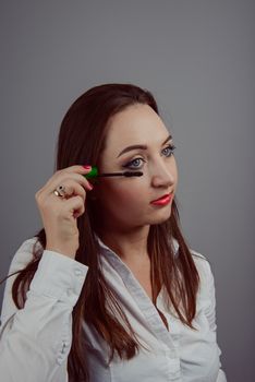Beauty model teenage girl looking in the mirror and applying mascara make up. Beautiful young woman apply makeup