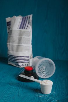 protein supplement powder in plastic spoon on blue wooden background