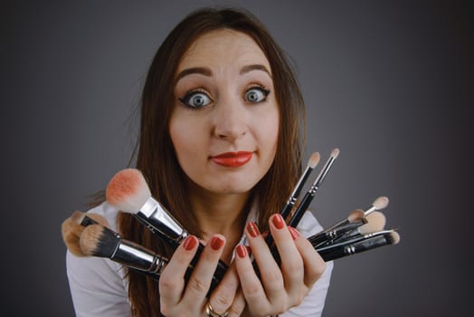 Woman holding a set of cosmetic brushes for make-up, isolated on gray
