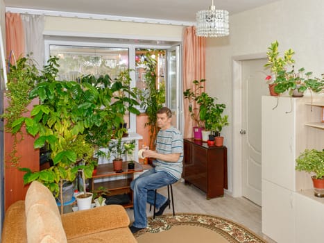 An elderly man in a bright room with home plants is engaged in his favorite hobby.