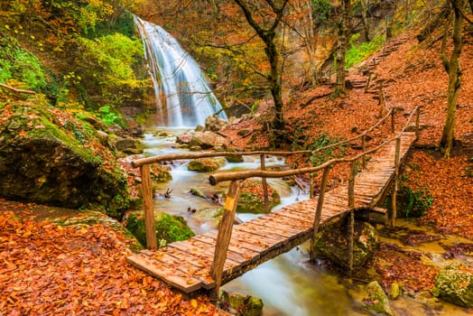 Postcard view of the picturesque waterfall Jur-Jur and the old wooden bridge, autumn Crimea, Russia